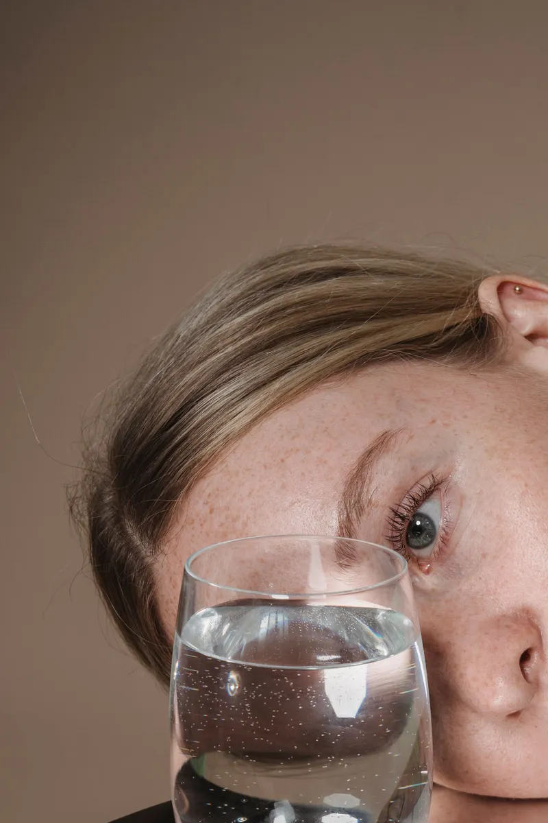 Vaso de agua transparente sostenido junto al rostro de una persona, bebida que no interrumpe el ayuno.