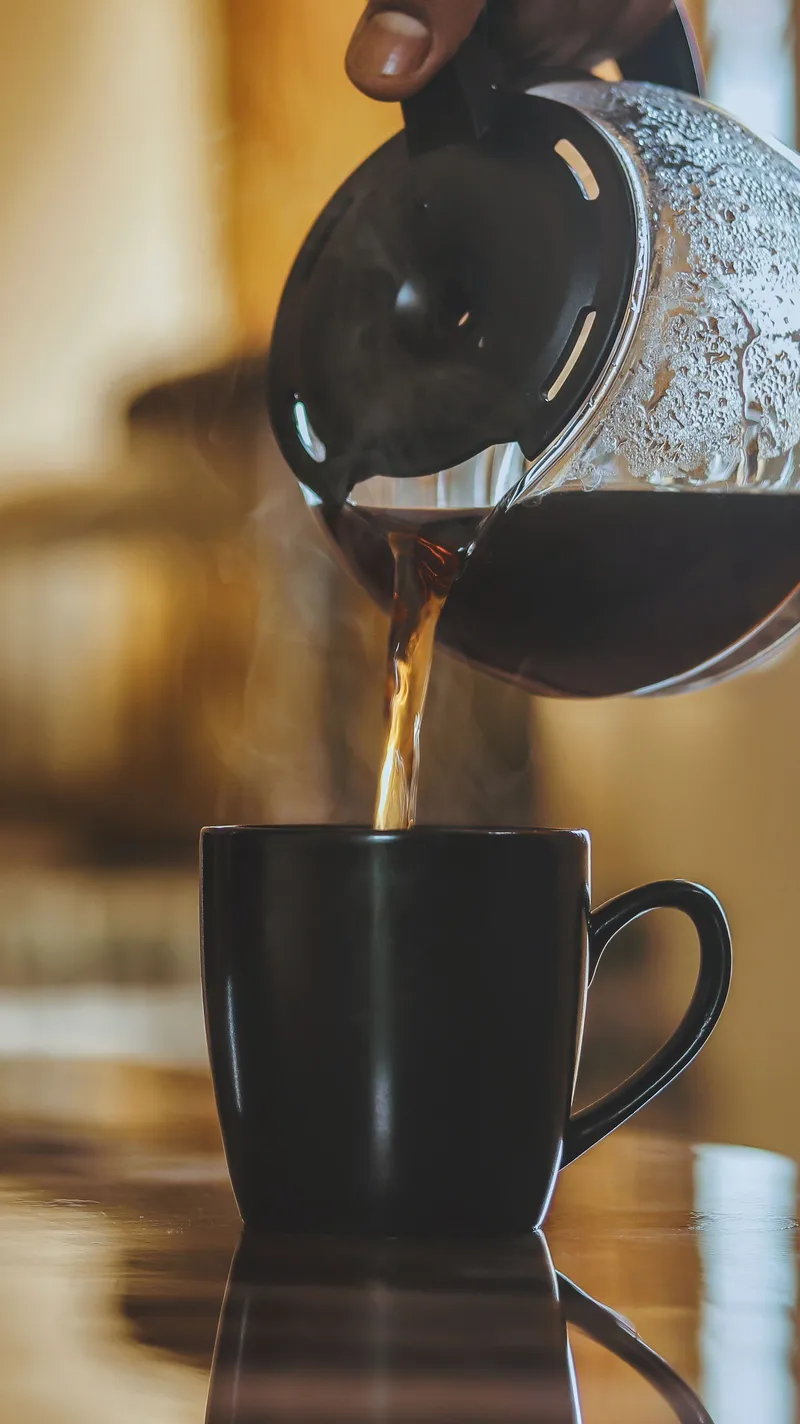 Café solo humeante servido en una taza negra desde una cafetera, apto durante el ayuno.