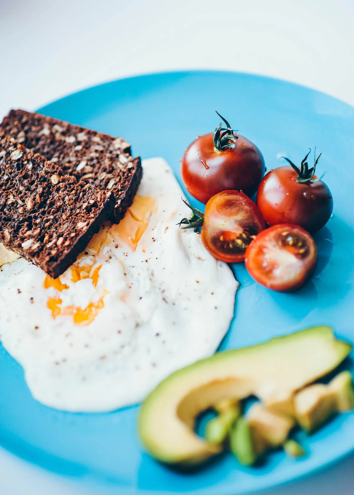Desayuno con huevo, pan integral, tomates cherry y aguacate en un plato azul para romper el ayuno de 12 horas