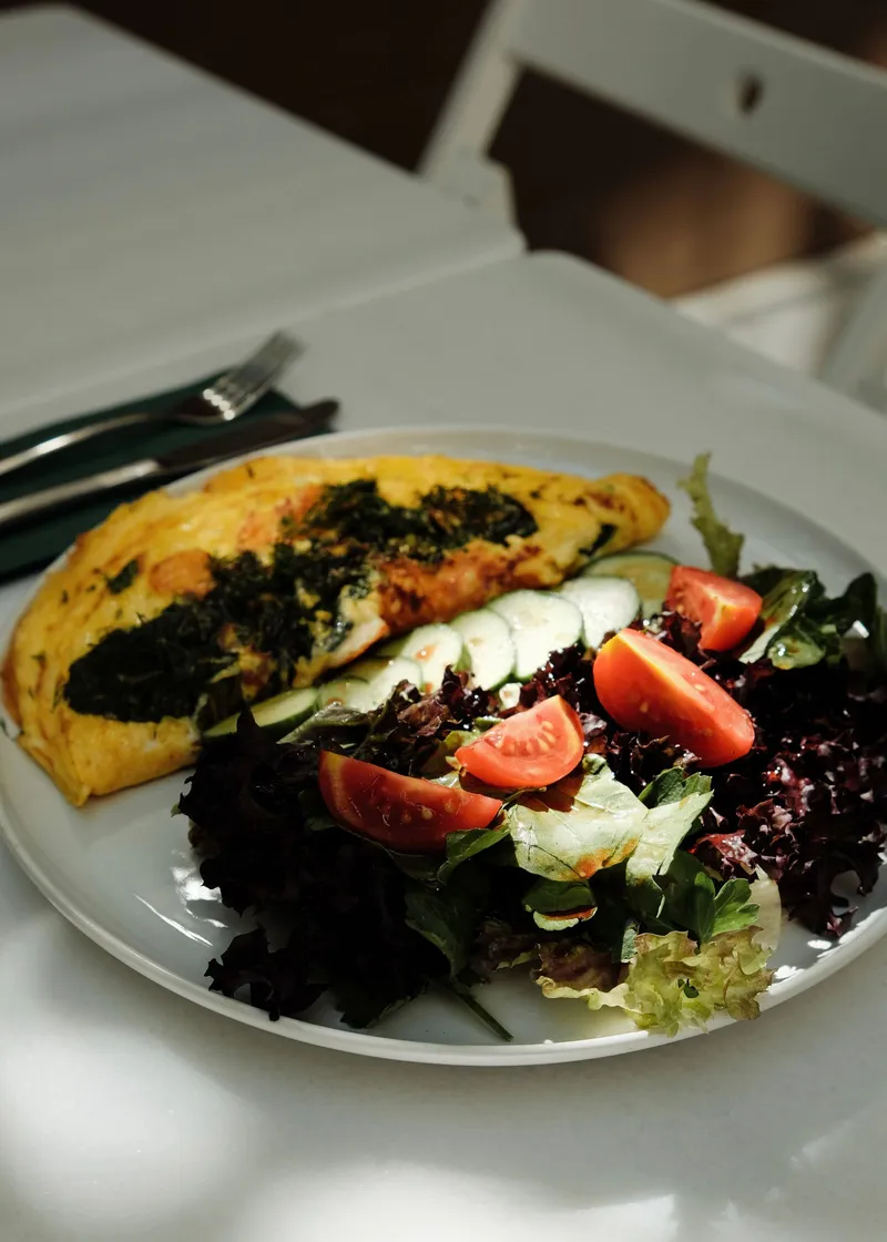 Tortilla francesa acompañada de ensalada verde y tomates en un plato blanco