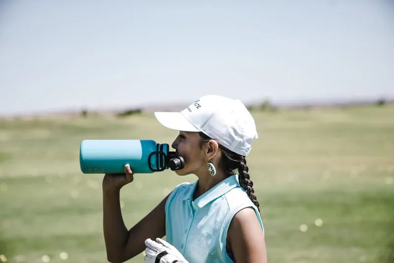 Persona bebiendo agua de una botella deportiva al aire libre bajo el sol