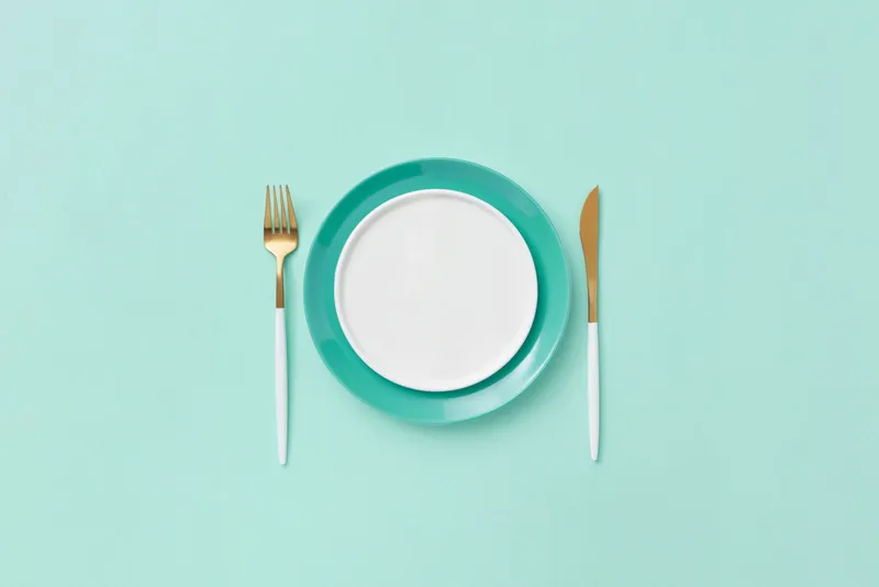 Plato vacío con tenedor y cuchillo sobre fondo turquesa, símbolo de la ventana de ayuno intermitente