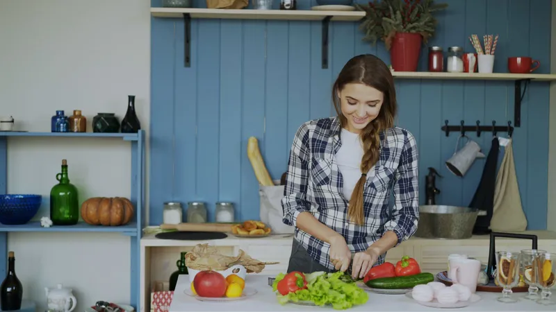 Mujer sonriente cortando verduras frescas en la cocina para planificar sus comidas dentro de la ventana de alimentación