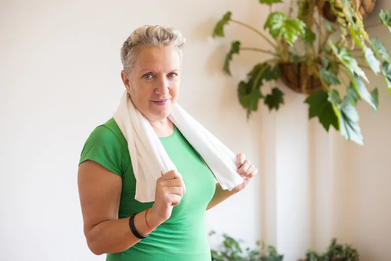 Mujer de mediana edad con camiseta verde y toalla al cuello tras entrenar en casa
