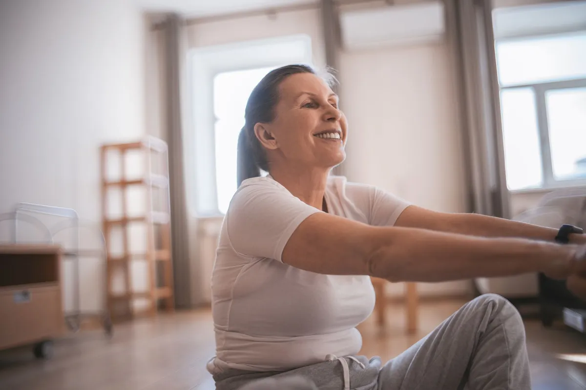 Mujer madura sonriente haciendo ejercicio en el salón de su casa durante la menopausia