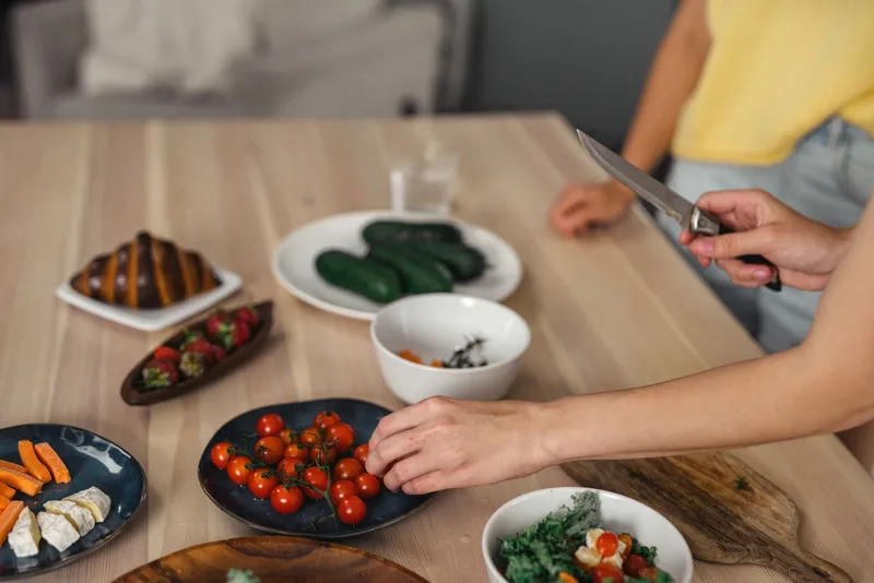 Persona cortando y organizando frutas y verduras frescas para preparar comidas saludables durante la ventana de alimentación