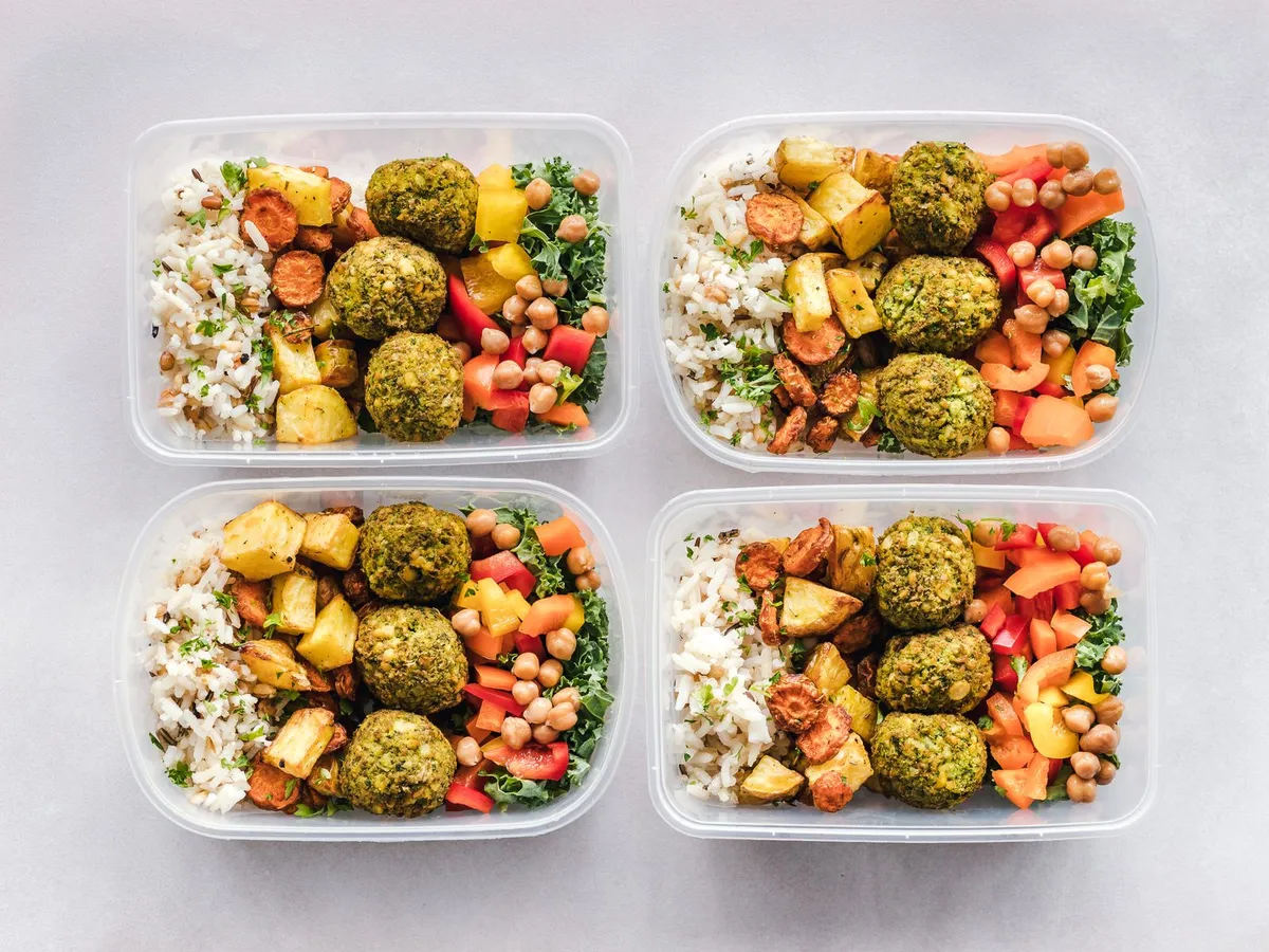 Cuatro tuppers de meal prep con falafel, arroz, garbanzos y verduras listos para empezar el ayuno intermitente
