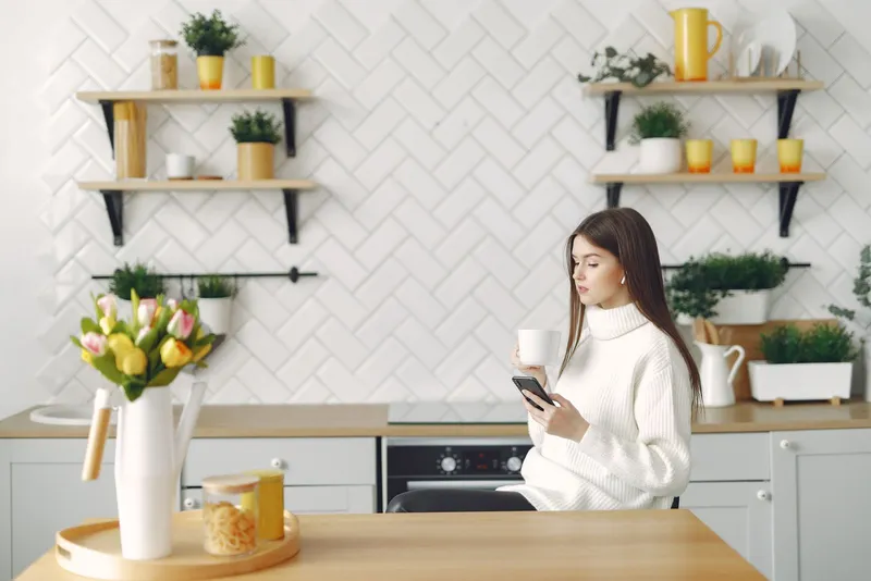 Mujer sonriente usa una app de ayuno en su teléfono sentada en la mesa de una cocina luminosa