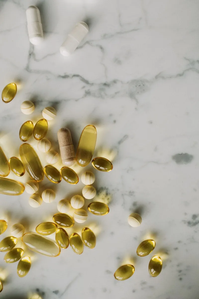 Cápsulas doradas de omega y comprimidos de vitaminas sobre una superficie de mármol