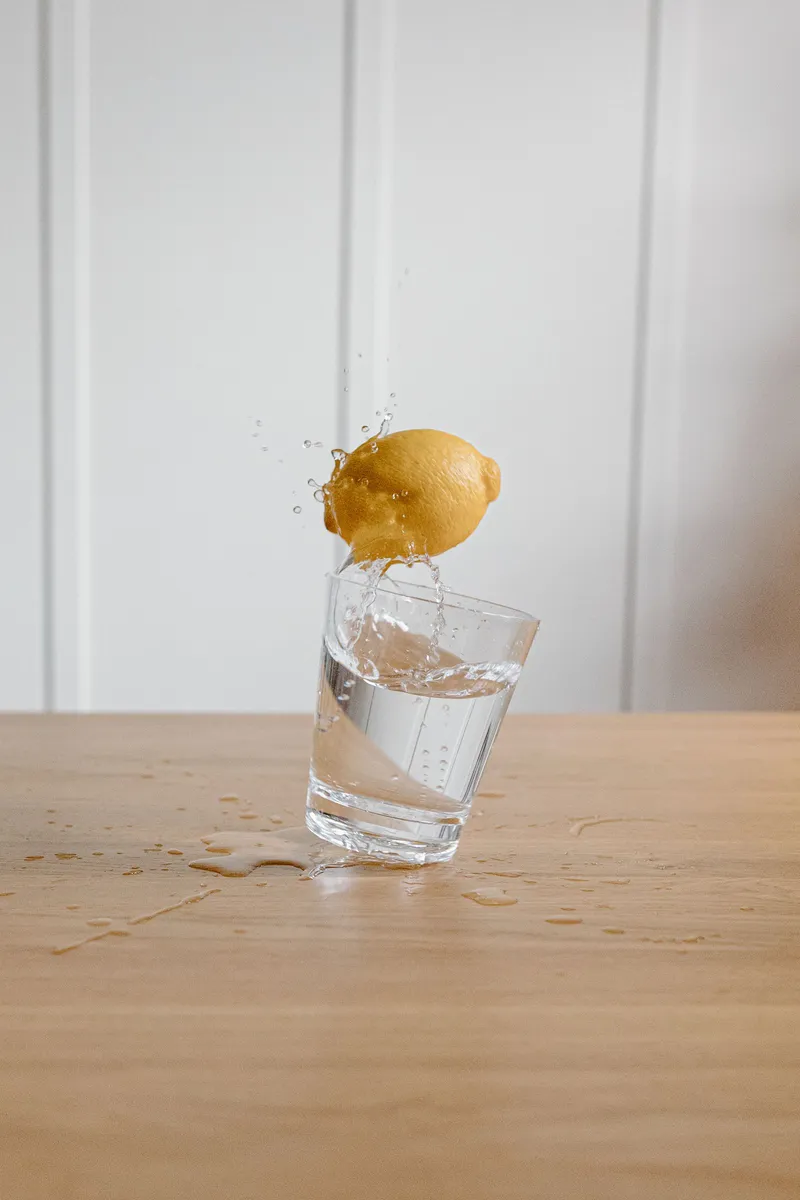 Un limón cae en un vaso de agua salpicando sobre una mesa de madera