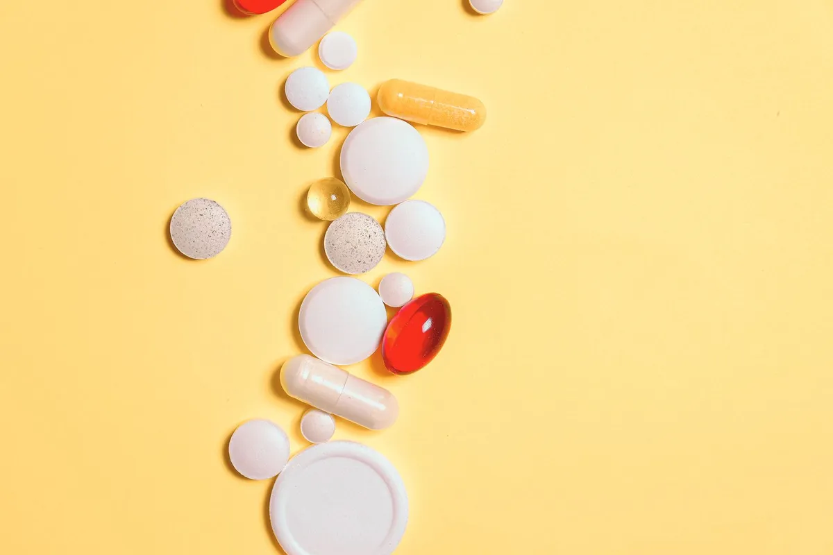 Variedad de pastillas, cápsulas y suplementos dispuestos sobre un fondo amarillo