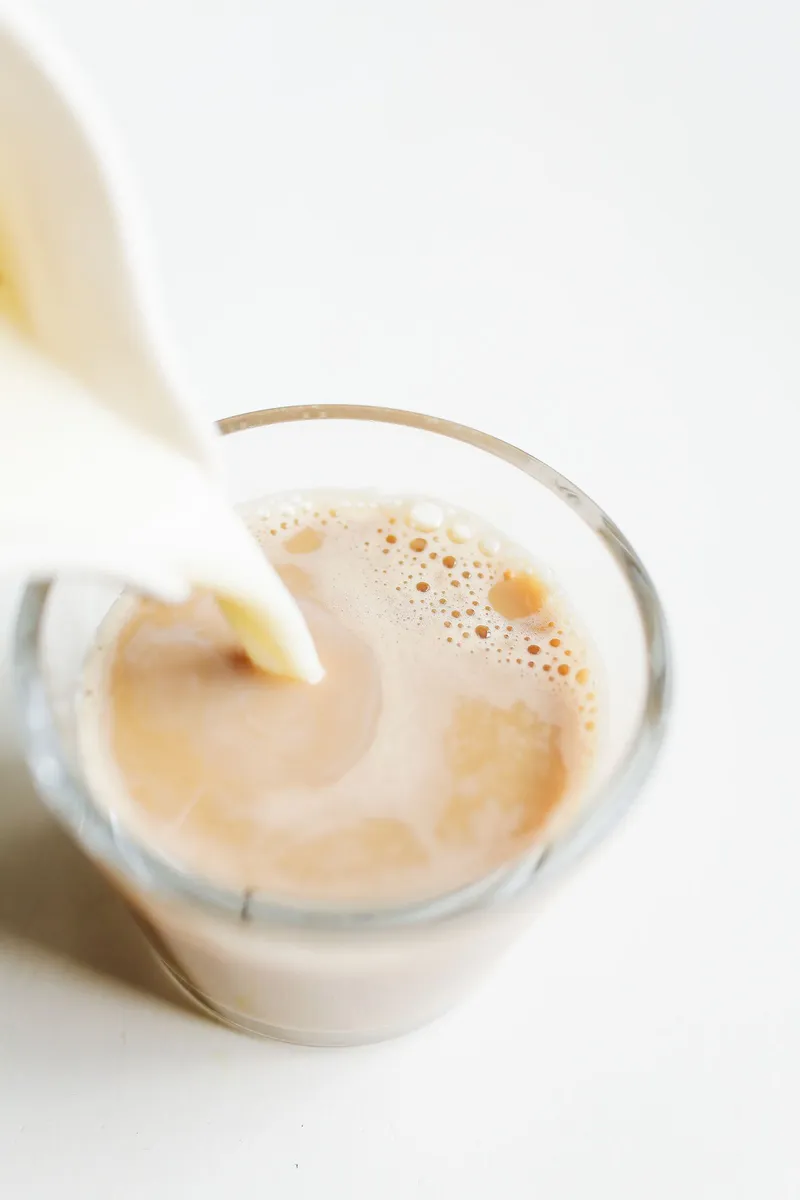 Leche cayendo dentro de un vaso de café con espuma sobre fondo blanco